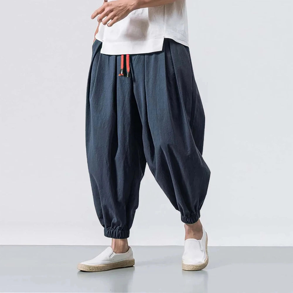Person wearing dark blue harem pants and white shoes on a light gray background