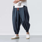 Person wearing dark blue harem pants and white shoes on a light gray background