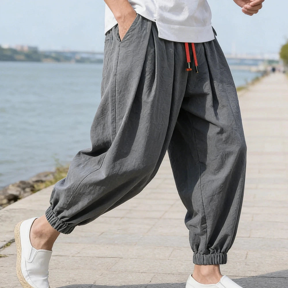 Person wearing gray wide-leg pants with a red drawstring, standing by a waterfront.