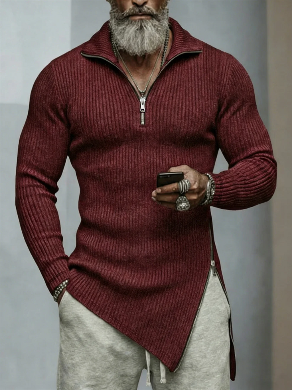 Man wearing a burgundy sweater with a zipper, holding a phone, against a neutral background