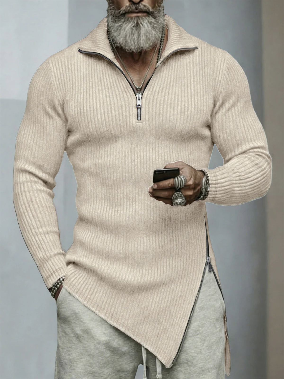 Man wearing a beige ribbed sweater with a zipper, holding a phone, on a gray background