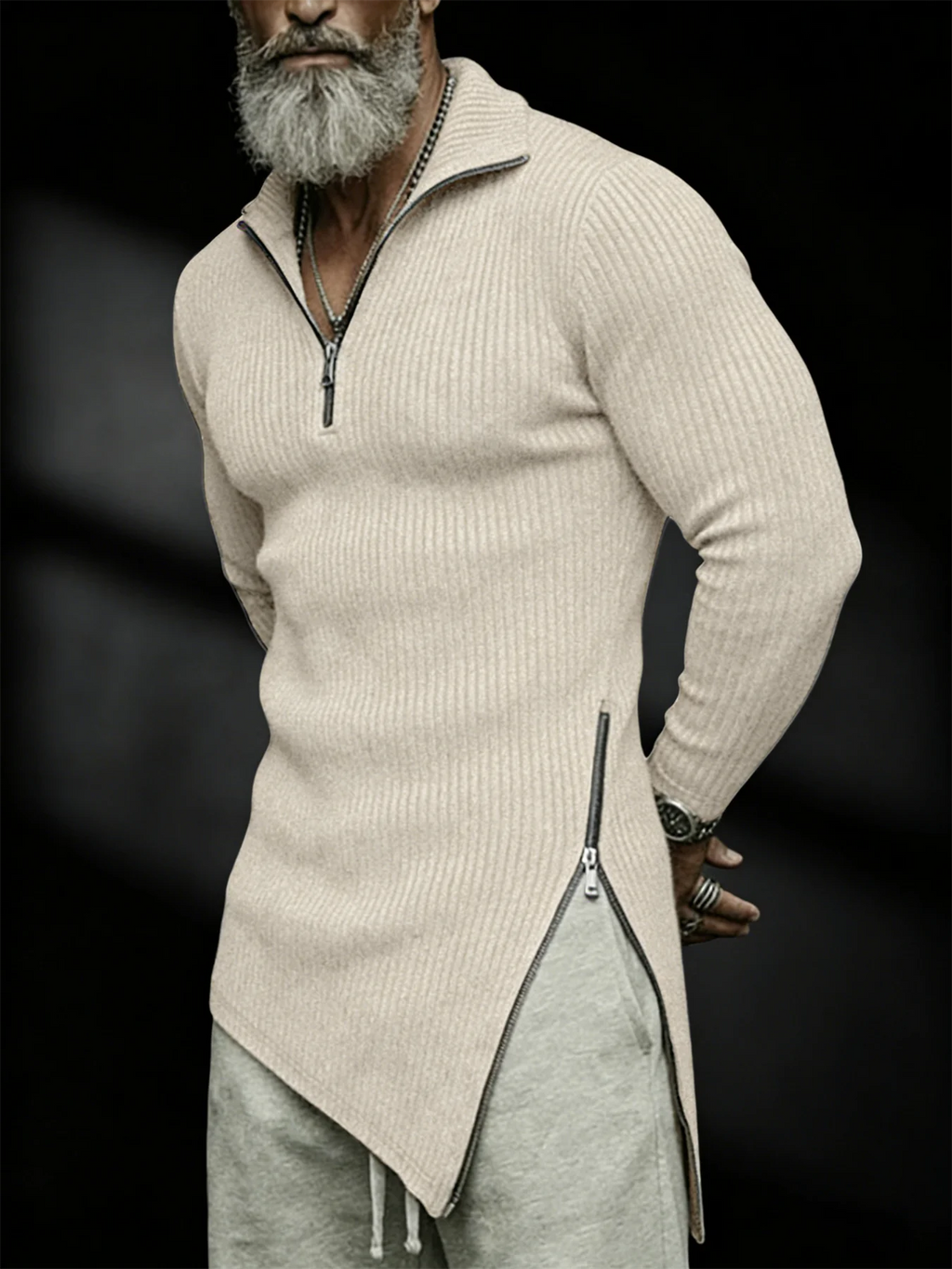 Man wearing a beige ribbed sweater with a zipper and gray pants on a black background