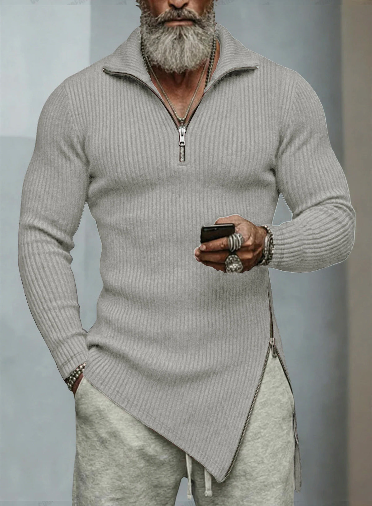 Man wearing a light gray zip-up sweater and pants, holding a phone.