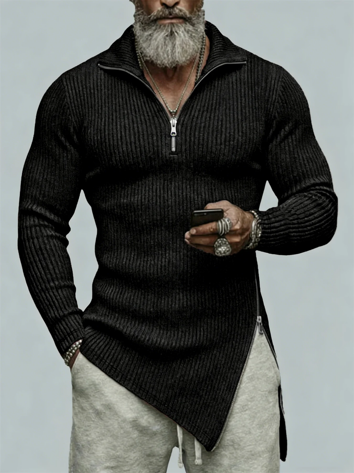 Man wearing a black sweater with a zipper, holding a phone, on a light gray background