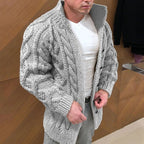 Man wearing a gray knitted cardigan over a white shirt in an indoor setting.