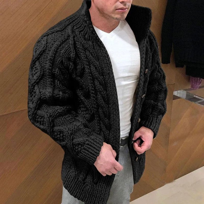 Man wearing a black cable knit cardigan over a white shirt in an indoor setting.