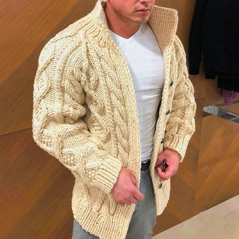 Man wearing a beige knitted cardigan over a white shirt in an indoor setting.