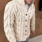 Man wearing a beige cable knit cardigan with brown buttons on a wooden floor.
