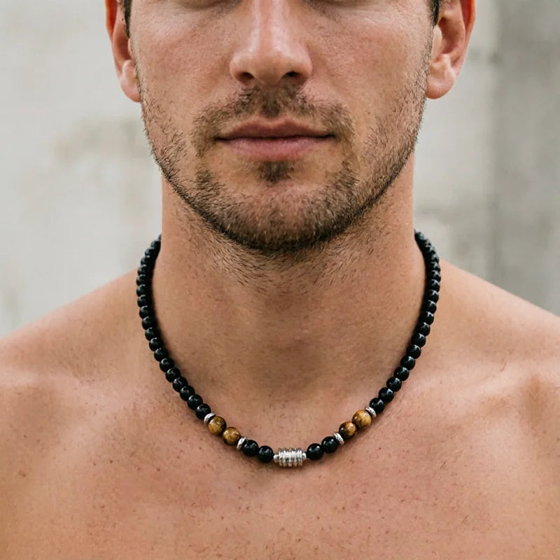 A close-up of a man's neck and lower face wearing a beaded necklace with black, brown, and silver beads.