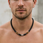 A close-up of a man's neck and lower face wearing a beaded necklace with black, brown, and silver beads.