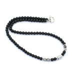 A beaded necklace featuring round black beads, a silver toggle clasp, and a few small gray and silver accent beads, displayed on a clean white background.