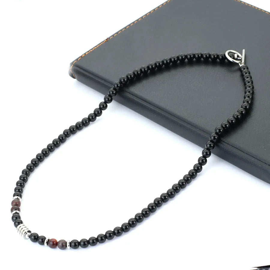 A black beaded necklace with a silver clasp, displayed on a black book against a white background.