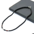A black beaded necklace with a silver clasp, displayed on a black book against a white background.
