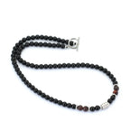 A beaded necklace featuring predominantly black round beads, accented with a few dark brown beads and silver-toned spacer and clasp details, displayed on a clean white background.