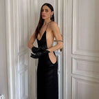 Woman in a black dress with a deep neckline and cut-out design, standing against a neutral wall.