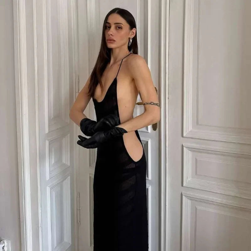 Woman in a black dress with a deep neckline and cut-out design, standing against a neutral wall.