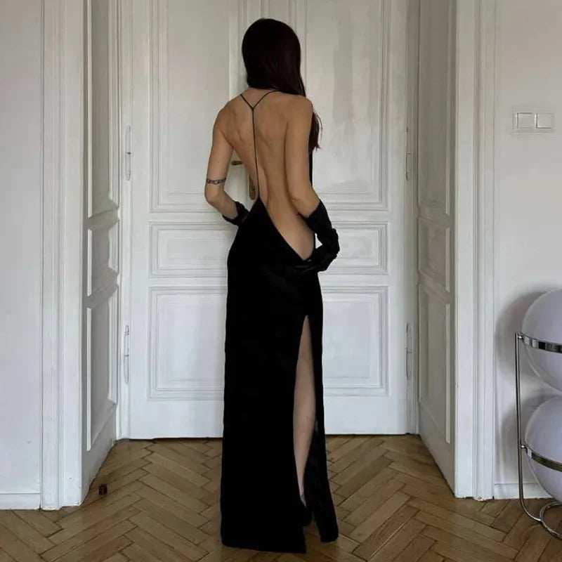 Woman in a black evening gown with a high slit and open back in an elegant room.