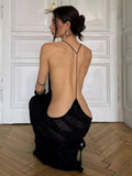 Woman wearing a black dress with thin straps kneeling in a room with white paneled walls.