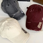 Three distressed baseball caps in gray, beige, and maroon on a white surface.