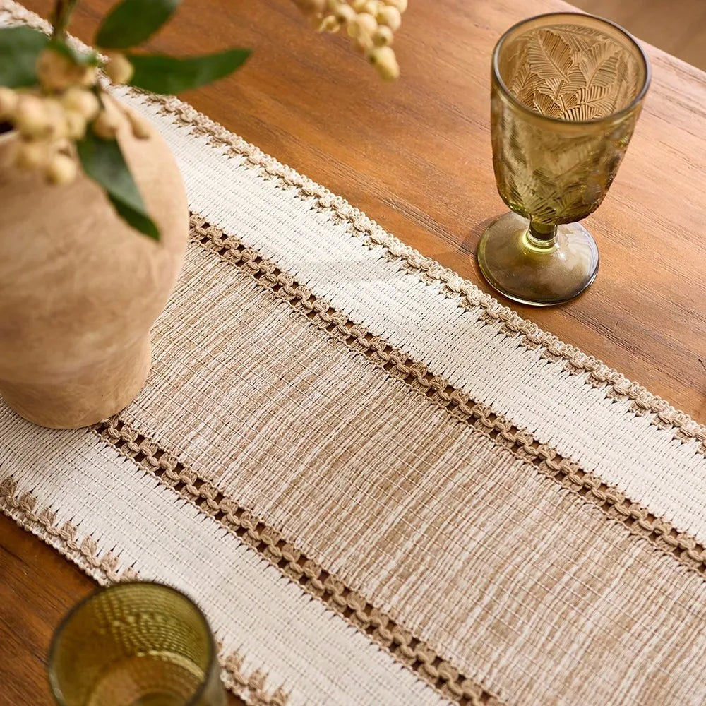 Textured table runner on a wooden table with decorative glasses and a vase.