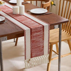 Dining table with a red and white patterned table runner, plates, and cutlery.