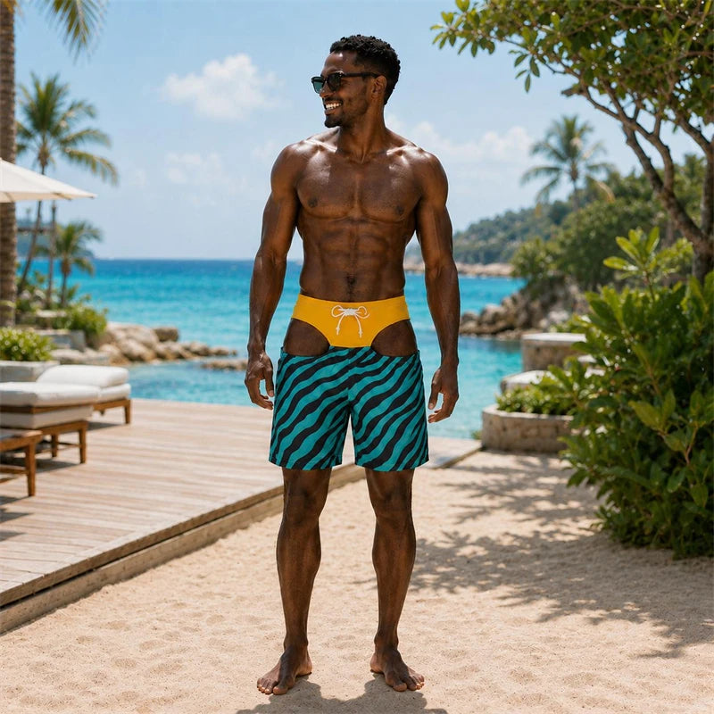 A muscular man wearing swim trunks stands on a sandy beach with a resort pool and ocean in the background. The swim trunks feature a yellow waistband with a white bow and a teal and black wavy patterned body.
