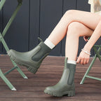 Person wearing green rubber boots with white socks sitting on a wooden floor.