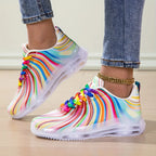 Colorful rain boots with rainbow patterns worn by a person on a light wooden floor.