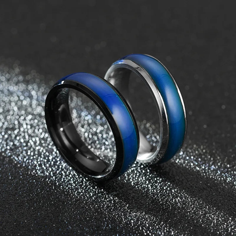 Two metallic rings, one black and blue, the other silver and blue, on a textured dark surface.