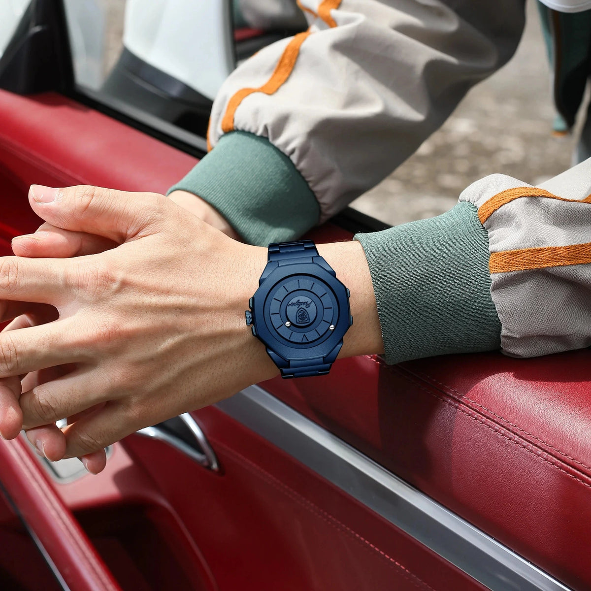 A person wearing a dark blue rugged sports watch with a matching blue strap, resting their hands on the red leather interior of a car.