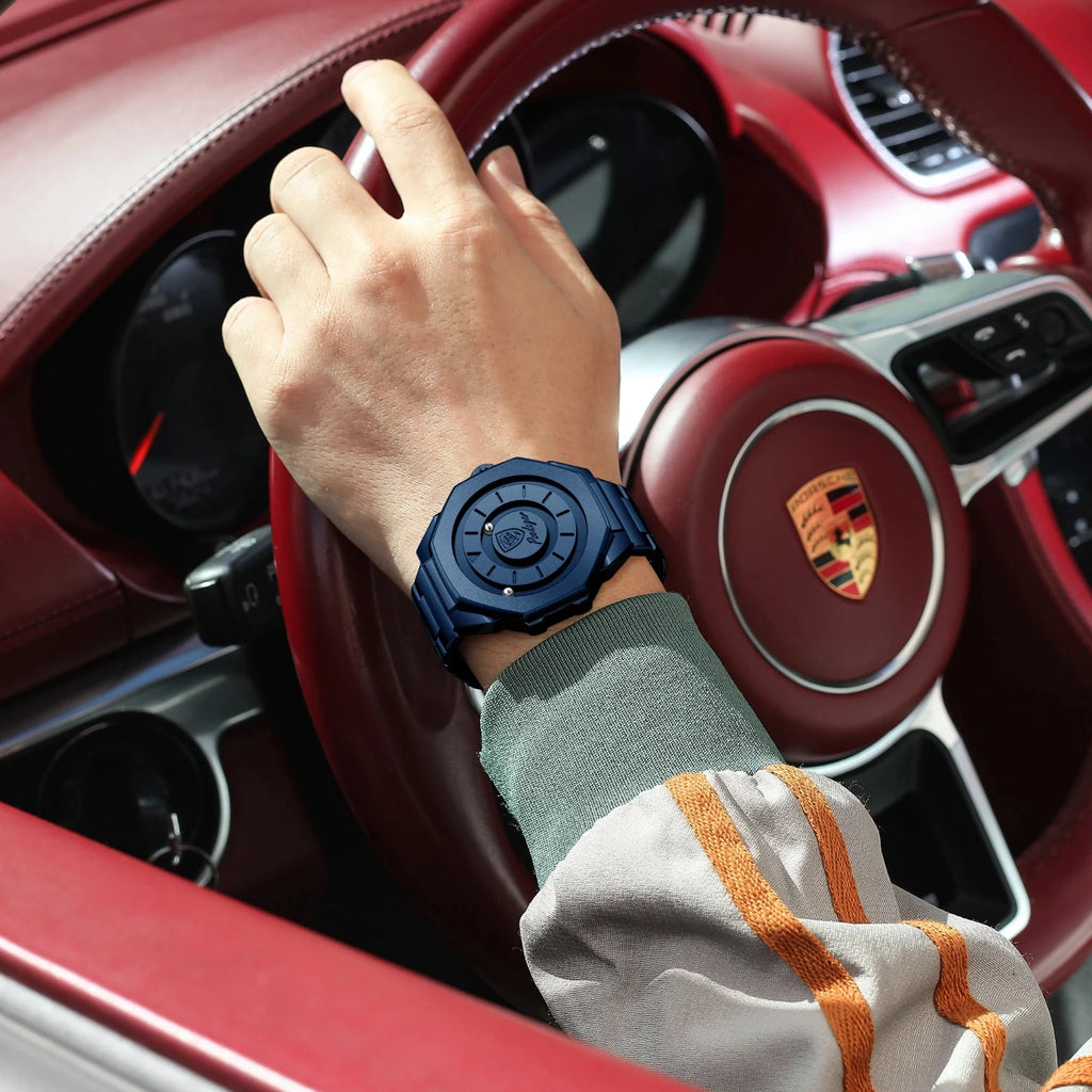 Hand wearing a blue watch on a car steering wheel with Porsche logo