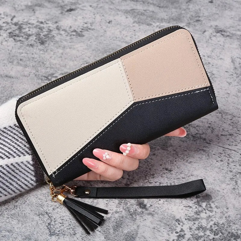 Color-blocked wallet with a tassel held by a hand on a textured surface