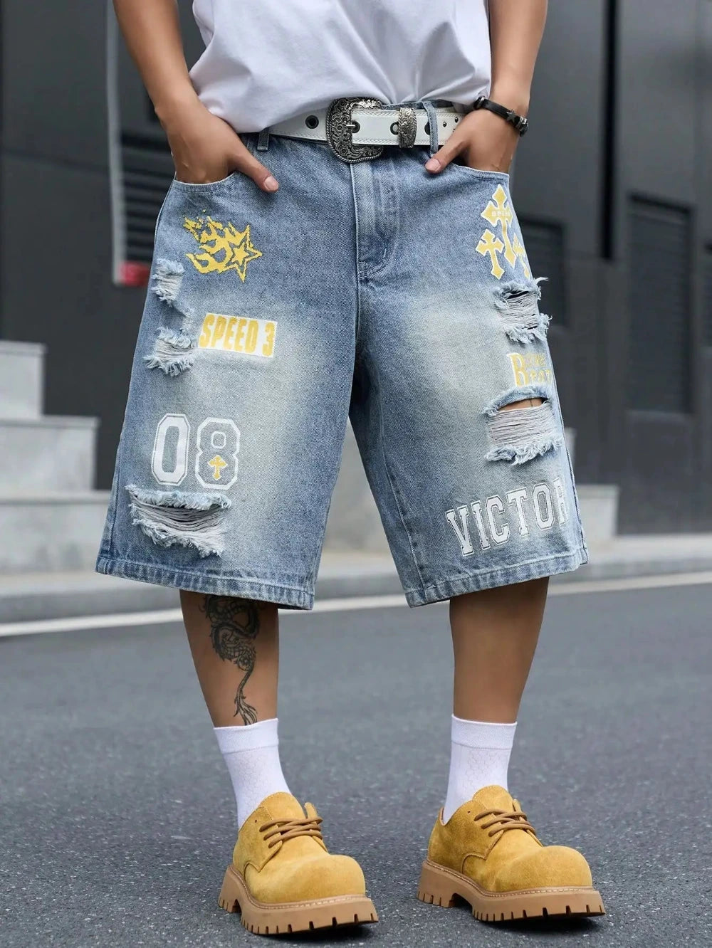 Light blue distressed denim shorts with yellow and white graphic patches, worn by a model with a white t-shirt, white socks, and yellow shoes.