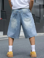 A person shown from the back wearing light-wash, wide-leg denim shorts with a faded wash, a white t-shirt, white socks, and mustard yellow slip-on shoes on an outdoor street.