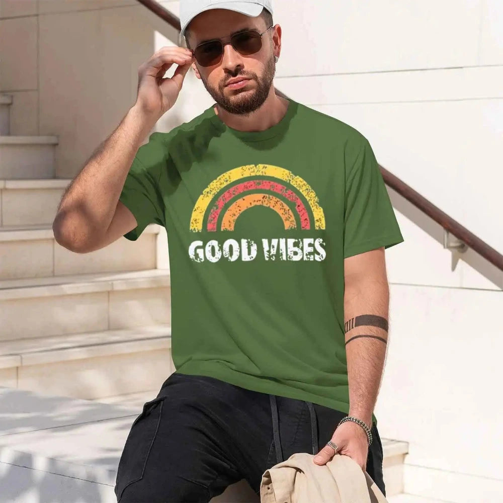 A man wearing a green crewneck t-shirt with a distressed rainbow graphic and the words 'GOOD VIBES' in white.