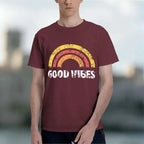 A man wearing a maroon burgundy t-shirt with a distressed retro rainbow graphic and the words 'GOOD VIBES' printed in white across the chest.