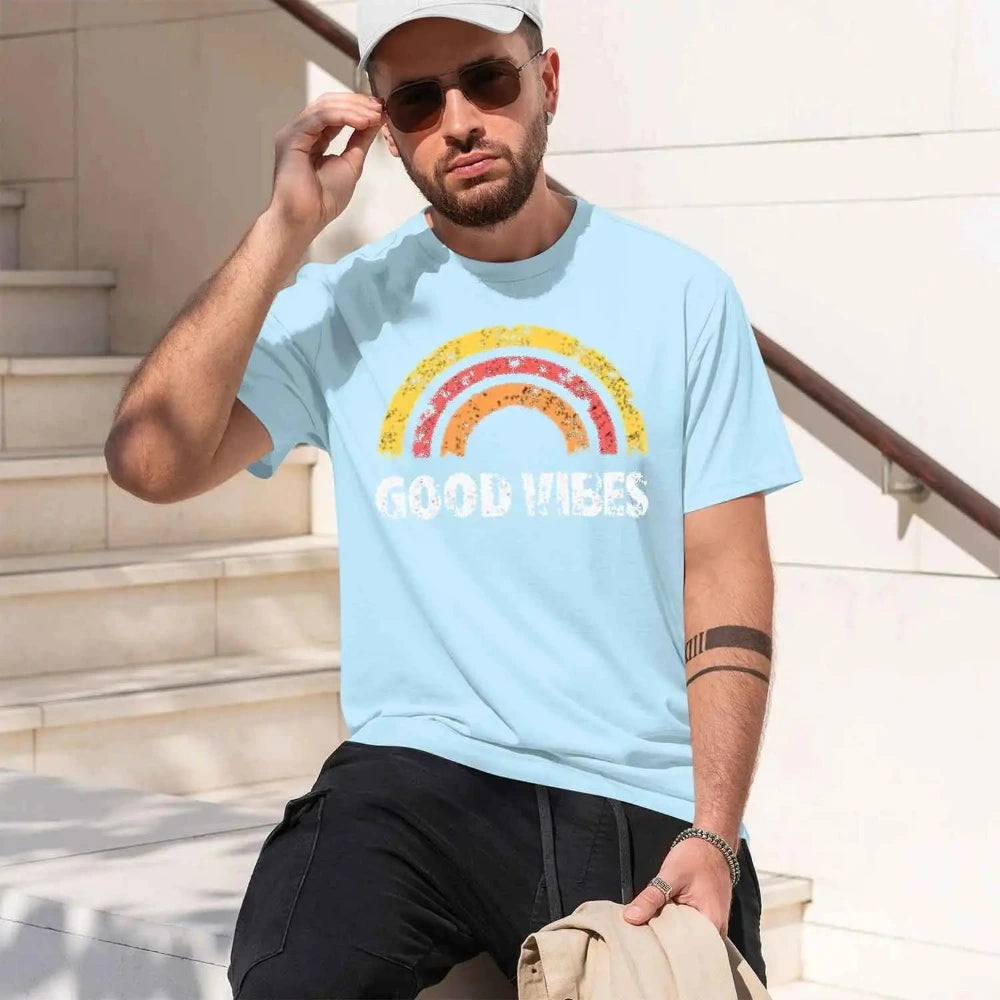 A man wearing a light blue crewneck t-shirt with a colorful distressed rainbow graphic and the words 'GOOD VIBES' printed in white. 