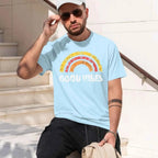 A man wearing a light blue crewneck t-shirt with a colorful distressed rainbow graphic and the words 'GOOD VIBES' printed in white. 