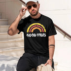 A man wearing a vintage black t-shirt with a retro rainbow graphic and the text 'GOOD VIBES' in white, sitting on outdoor stone steps.