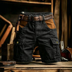 Black cargo shorts with brown leather accents, including a matching belt, a side leather strap, and brown contrast panels on the front pockets, displayed on a rustic wooden surface.