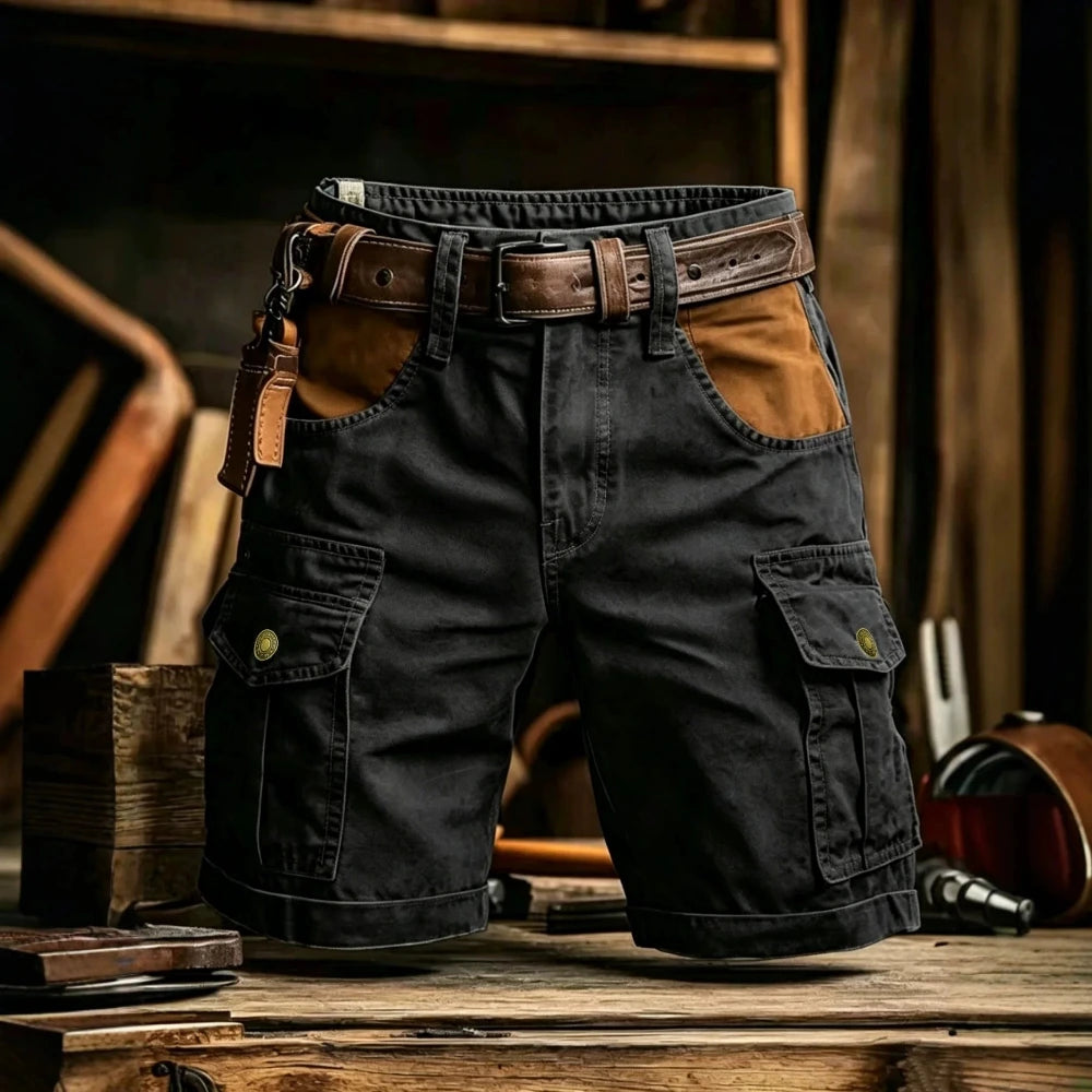 Black cargo shorts with brown leather accents, including a matching belt, a side leather strap, and brown contrast panels on the front pockets, displayed on a rustic wooden surface.