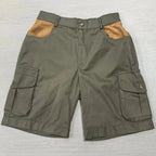 A pair of olive green cargo shorts with tan contrast panels on the back pocket tops, laid flat on a light gray wood-textured surface.