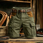 Olive green cargo shorts with brown leather accents, including a matching belt and a leather key fob, displayed on a rustic wooden table.