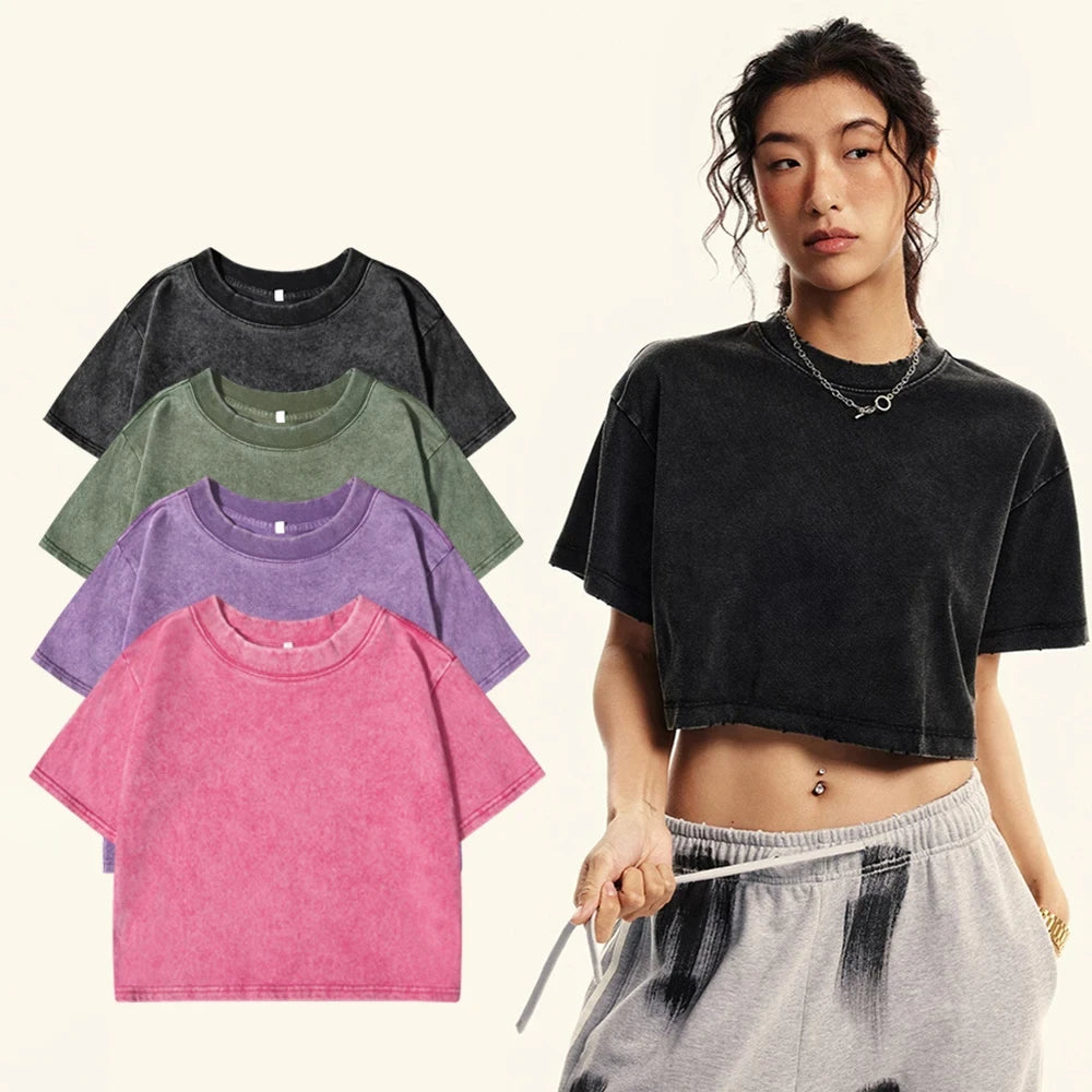 A model wears a black acid-wash cropped t-shirt, with four other color options (black, green, purple, pink) displayed on the left against a light cream background.