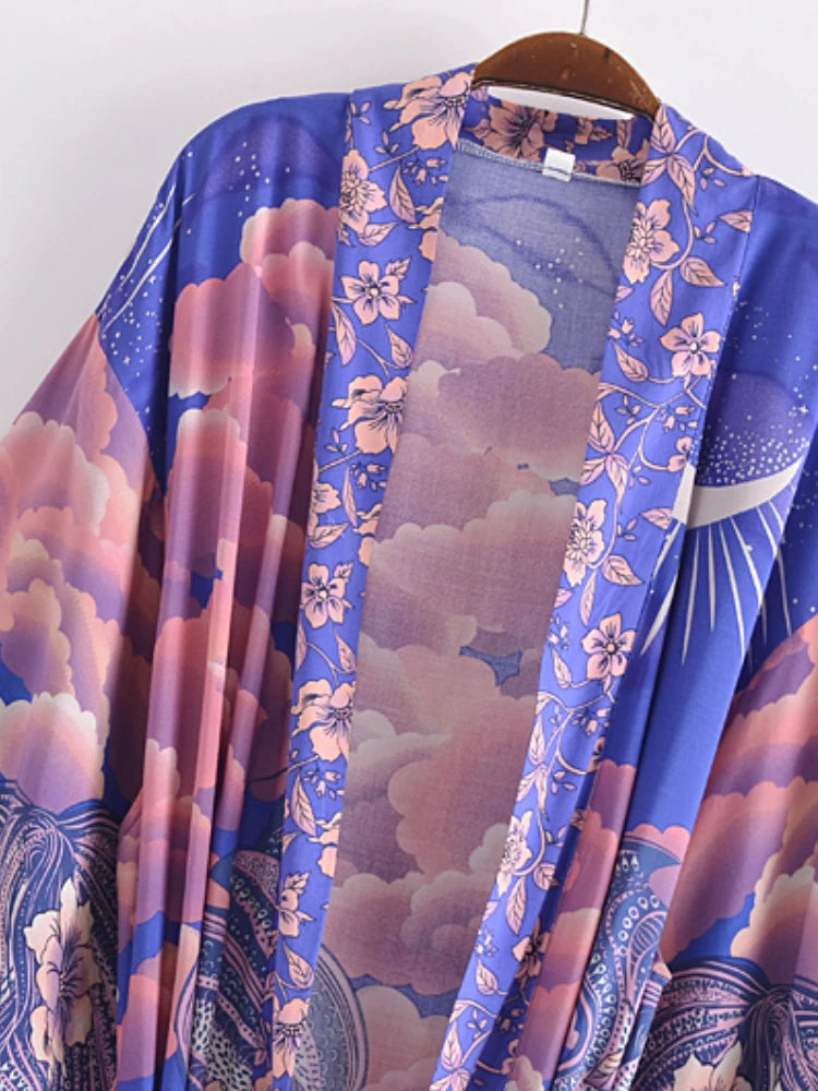 A lightweight open-front kimono-style cardigan draped on a wooden hanger, featuring a vibrant purple and pink floral cloud print with celestial and wave motifs.