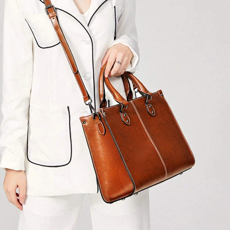 Brown leather handbag held by a person wearing a white outfit on a light gray background