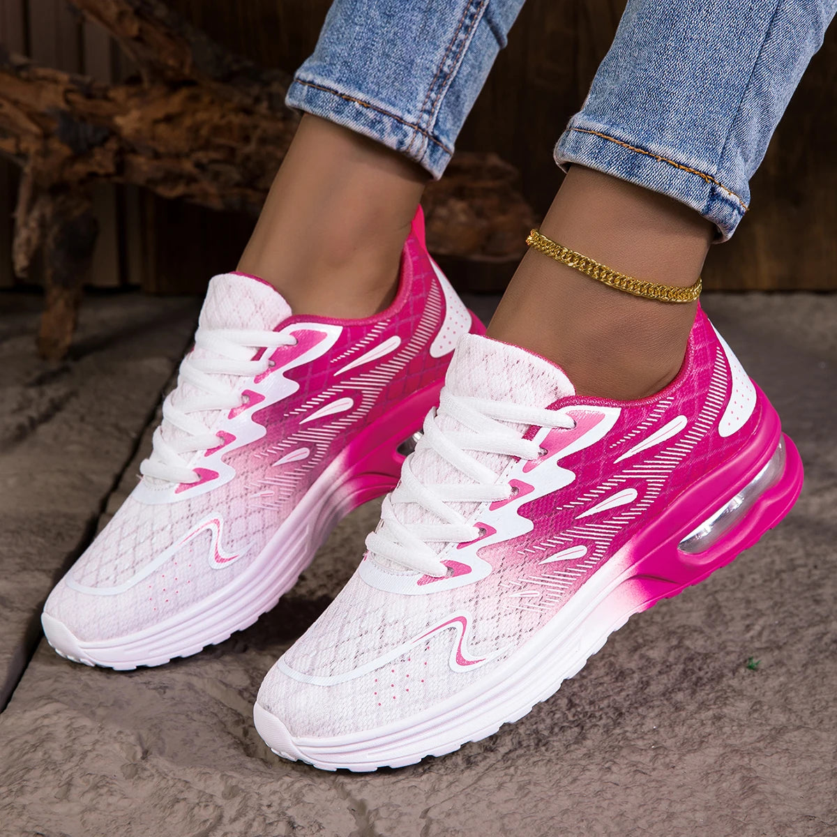 White and pink sneakers worn with rolled-up jeans on a stone surface.