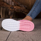 Close-up of a shoe with a white sole and pink heel on a textured surface.