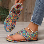 Colorful patterned sandal being worn on a wooden floor.