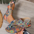 Colorful floral-patterned sandals being worn on a wooden floor.